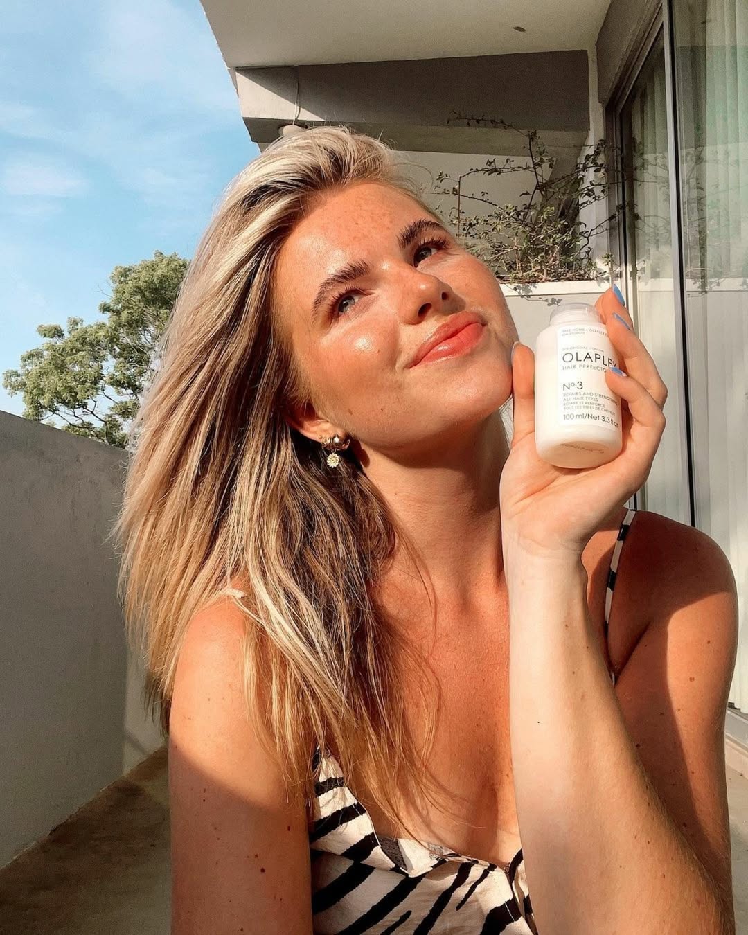 Influencer holding a bottle of Olaplex hair treatment on a sunny balcony